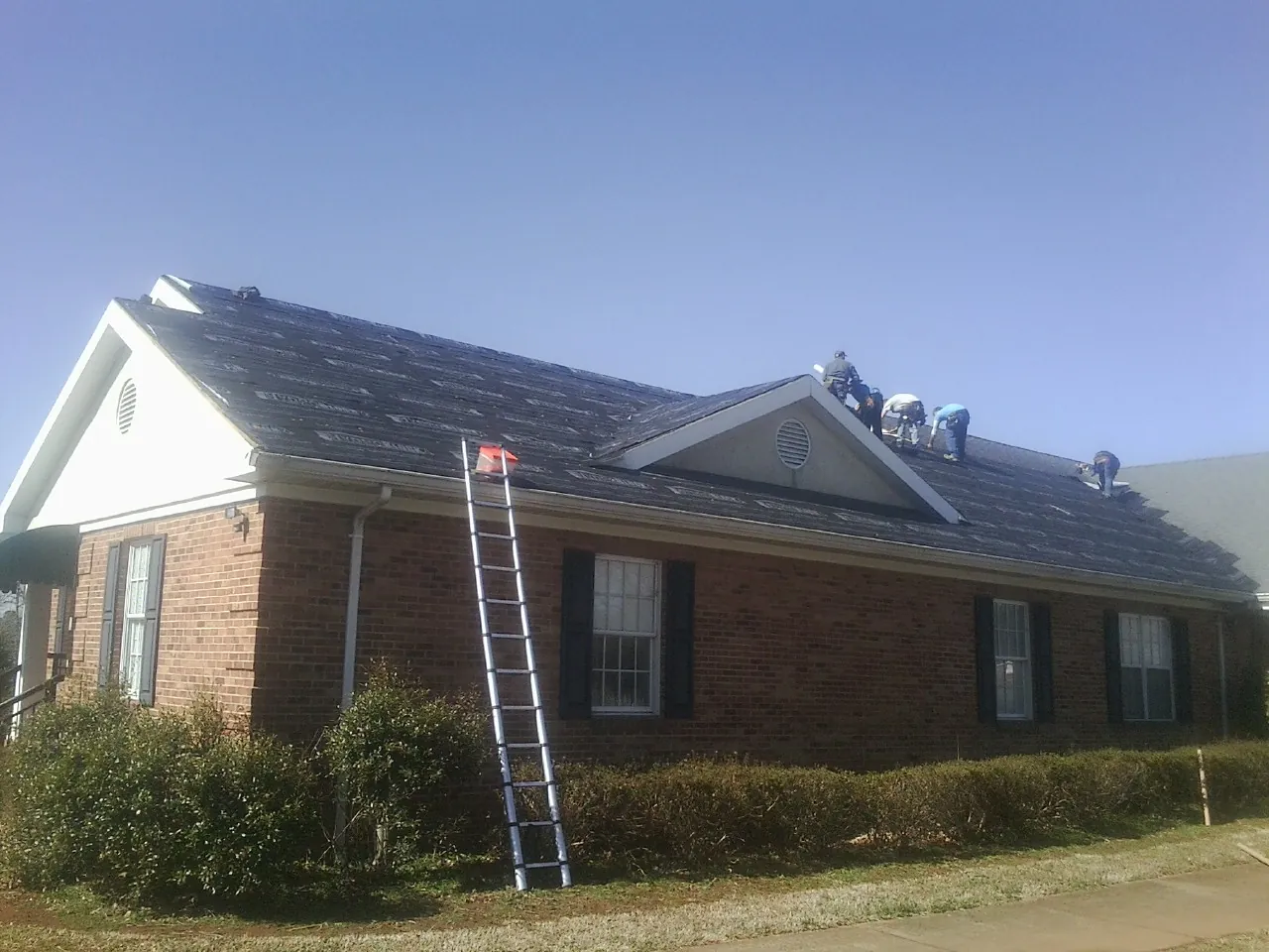 Crew tearing shingles off a brick ranch roof with a ladder set — Emergency Roof Repair work by our crew in University Park